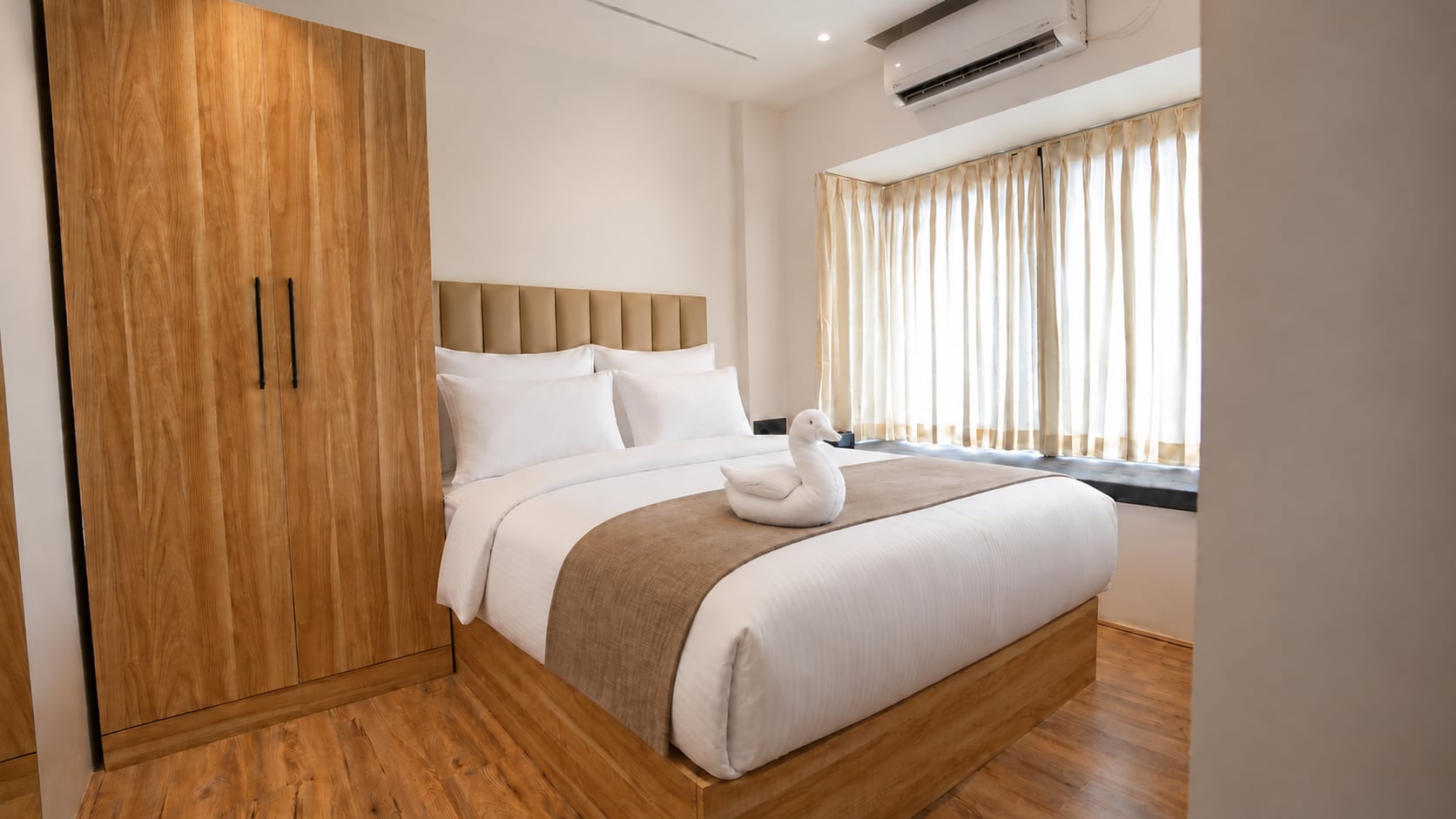Sunlit Old Mill guest room with crisp white bedding, a towel swan and warm timber finishes