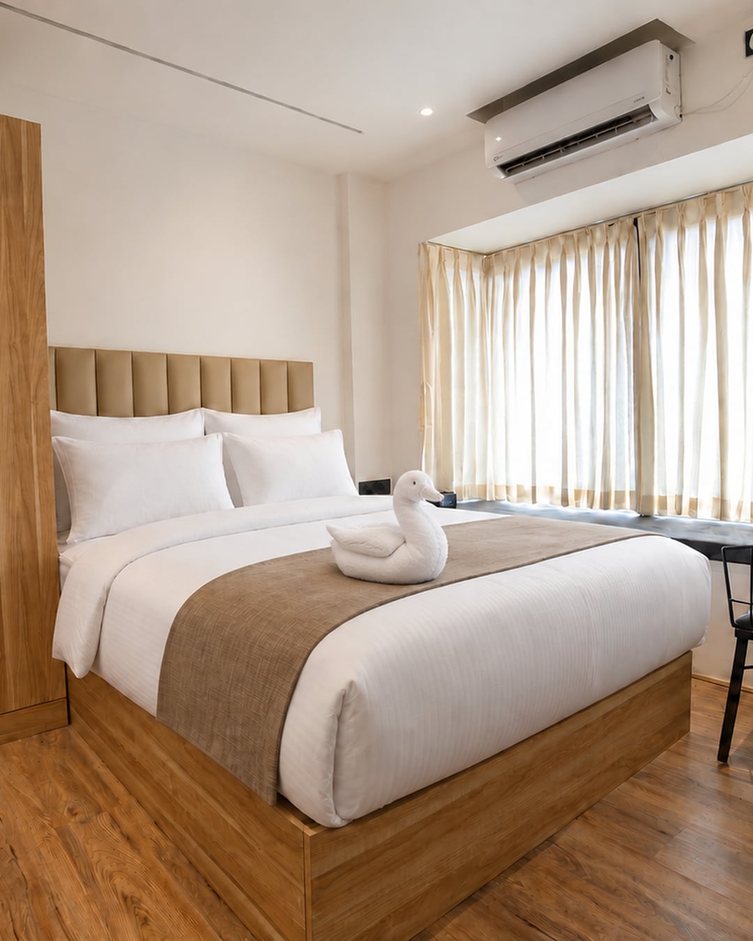 Sunlit Old Mill guest room with crisp white bedding, a towel swan and warm timber finishes