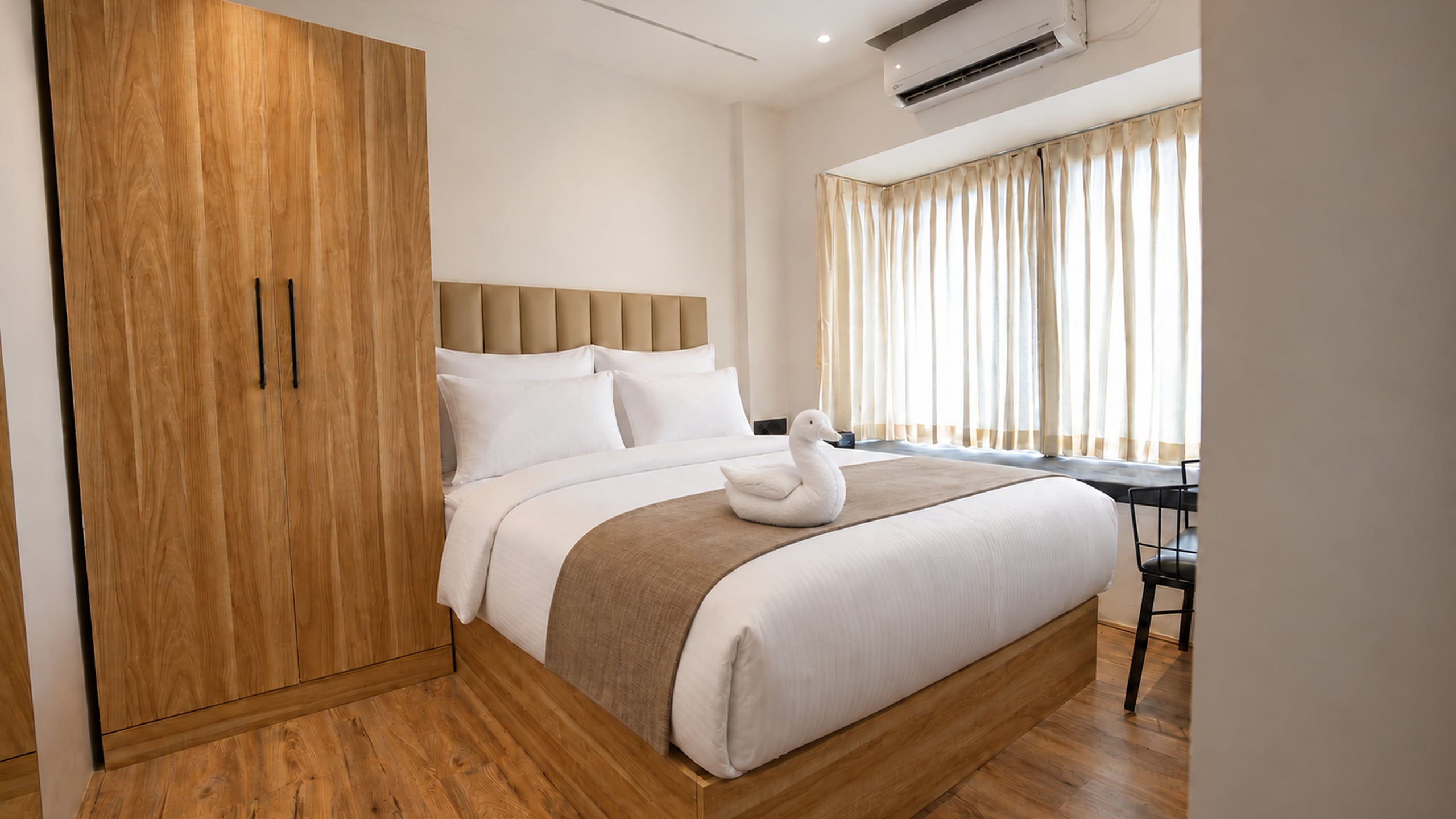 Sunlit Old Mill guest room with crisp white bedding, a towel swan and warm timber finishes
