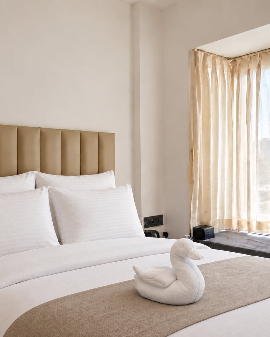 Crisp pillows, an upholstered headboard and a towel swan beside the guest-room window