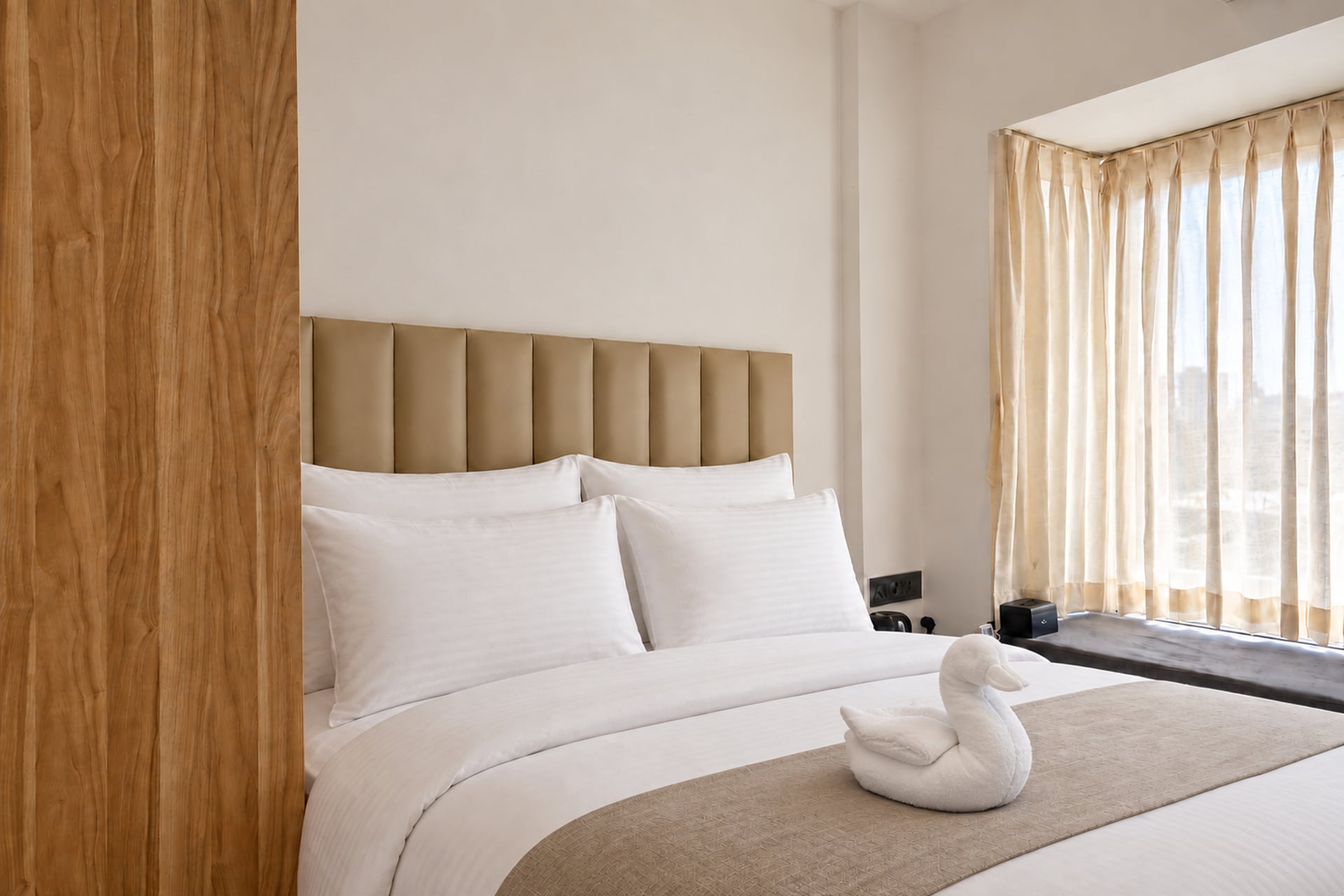 Crisp pillows, an upholstered headboard and a towel swan beside the guest-room window